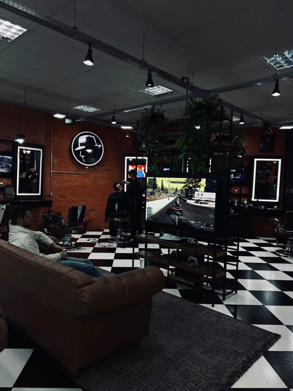 Lounge com PS5, telão e parede de tijolos da La Mafia Petrópolis